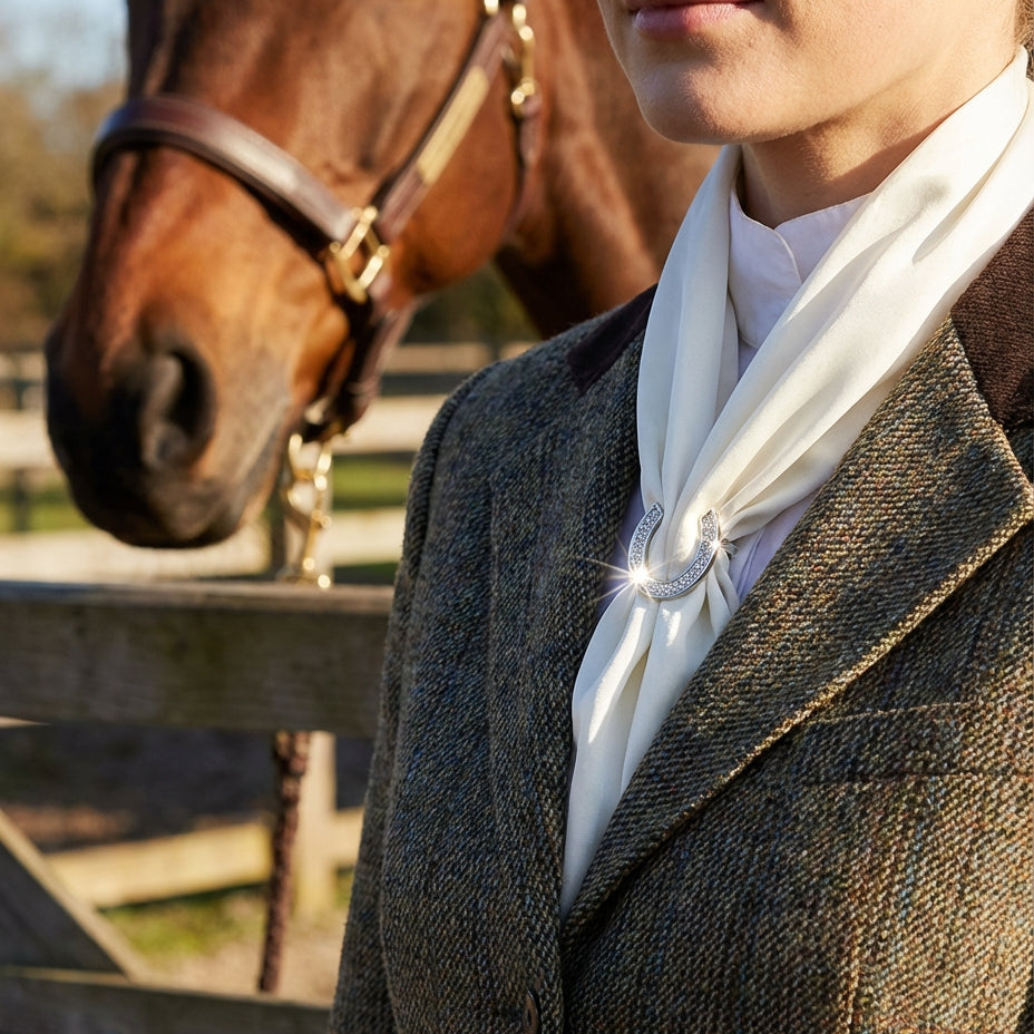 Person wearing a dark coat with a white scarf standing next to a horse.